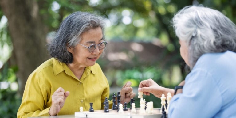 Two Elderly Women Playing Chess Together Outdoors at an Assisted Living Facility